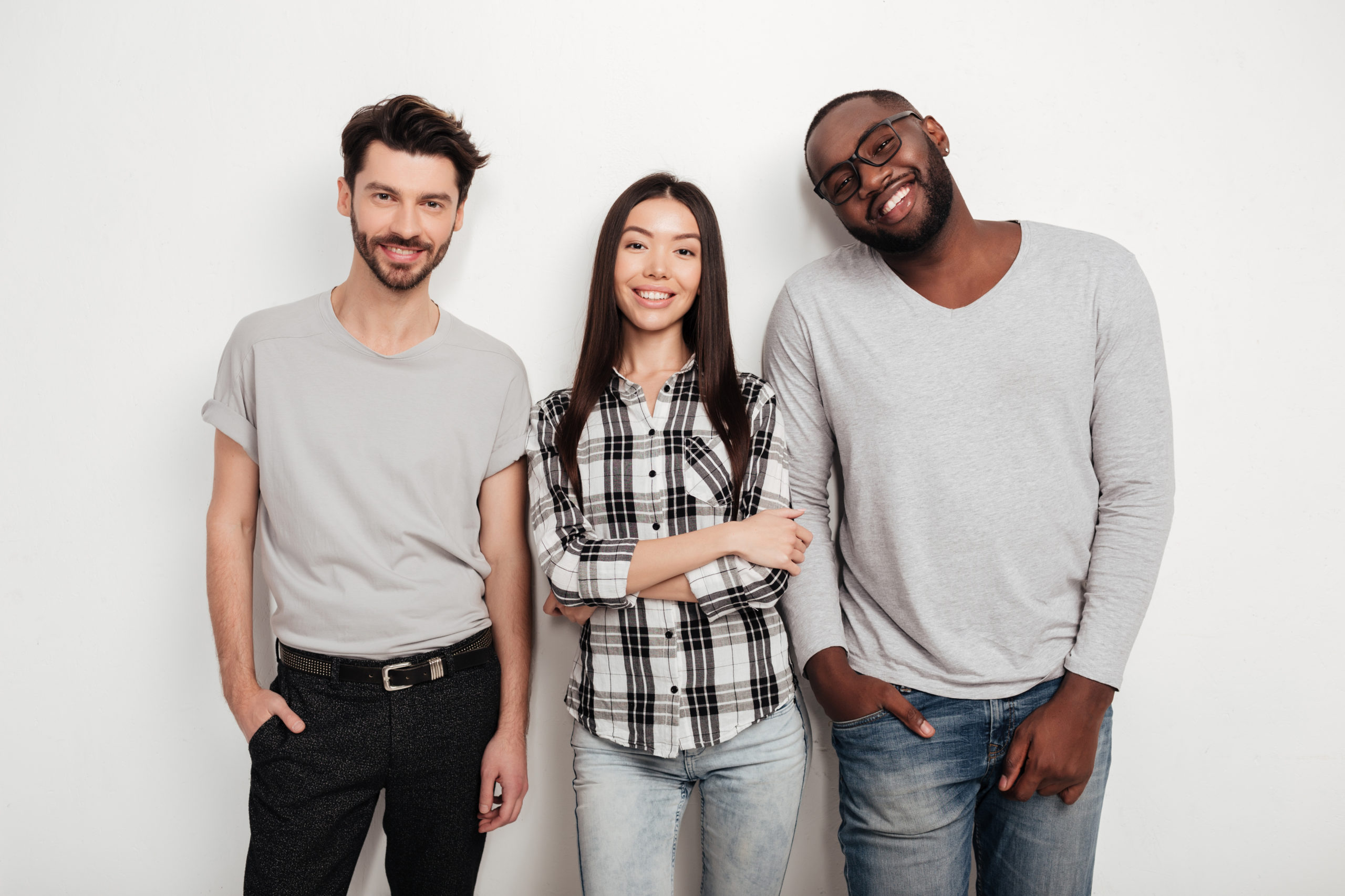 portrait-three-multinational-friends-standing-together-joyfully-looking-camera-white-background-studio